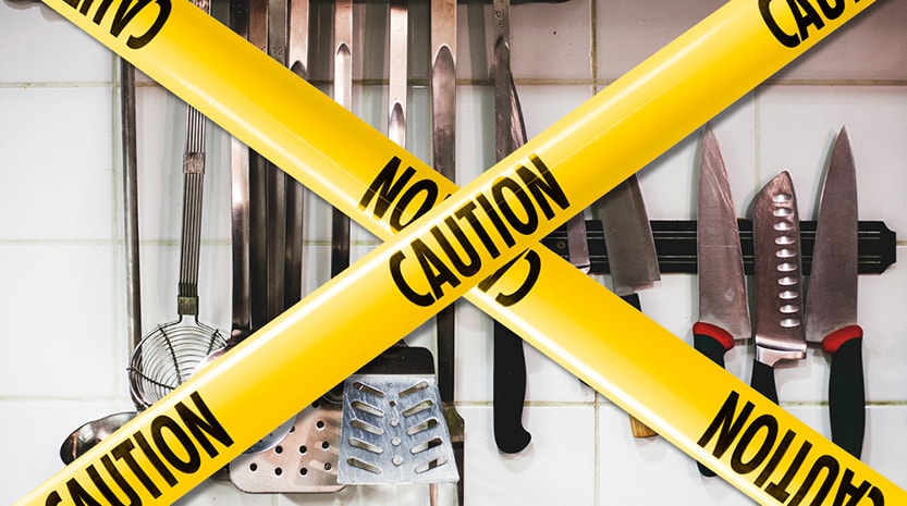 Caution tape is strung over various kitchen tools hanging on a tile wall.