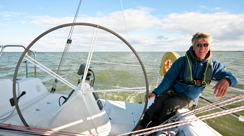 A man pleasantly leans against the edge of his boat on the lake while steering his boat with one hand.