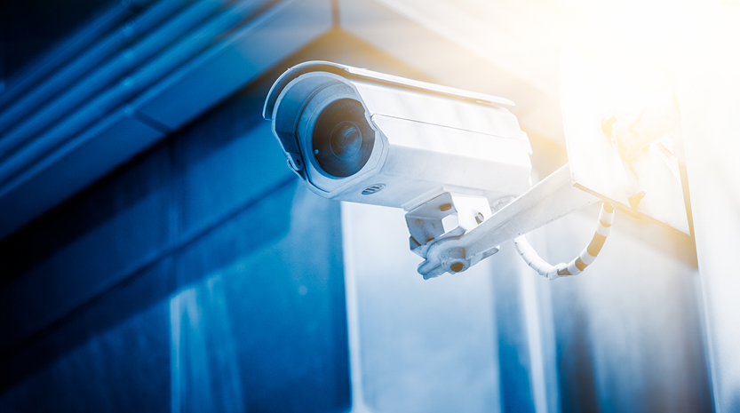 A sunny photo of a security camera on the side of a building.
