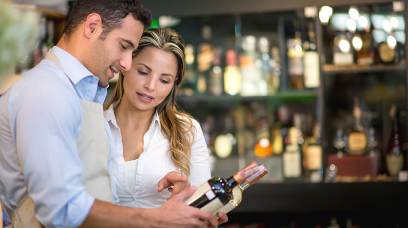 Man and woman hold bottles of wine and discuss the labels while in a winery.