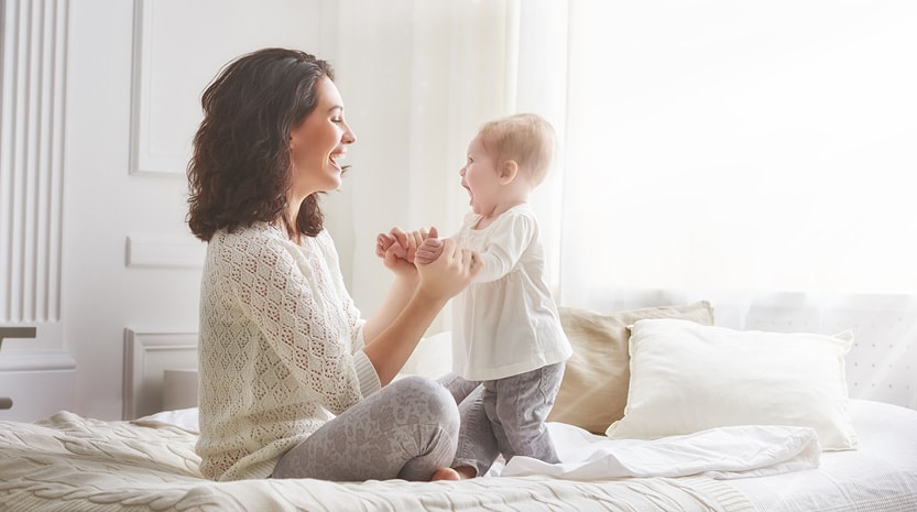 A young mother sitting on her bed playing with her baby.