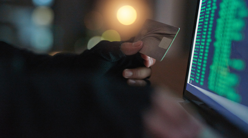 A criminal holding stolen credit card in front of a computer screen.